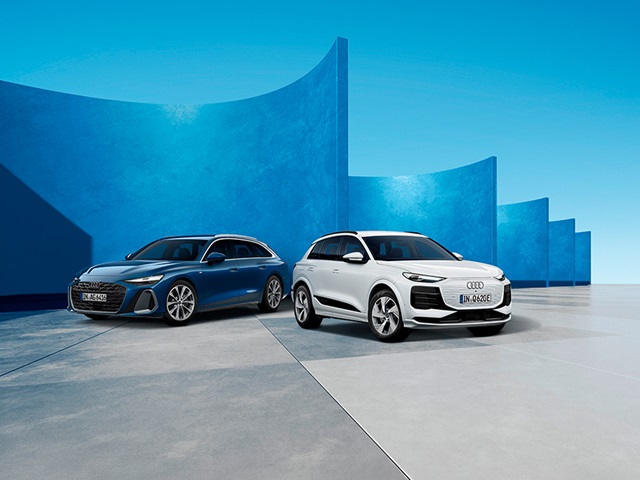 Zwei Audi-SUVs, ein weißer und ein blauer, stehen vor einer modernen, blau gestrichenen Wand mit geschwungenen Formen