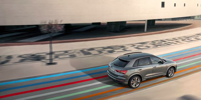 Audi Q3 fährt durch eine moderne Stadtstraße mit buntem Hahn Code.