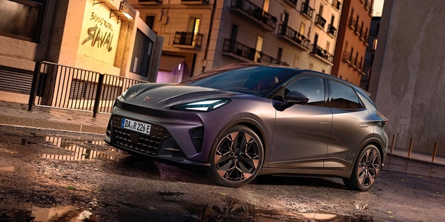 Seitenansicht eines CUPRA Raval Elektroautos in mattem Dunkelgrau vor urbaner Kulisse mit nassen Straßen und Gebäuden im Hintergrund