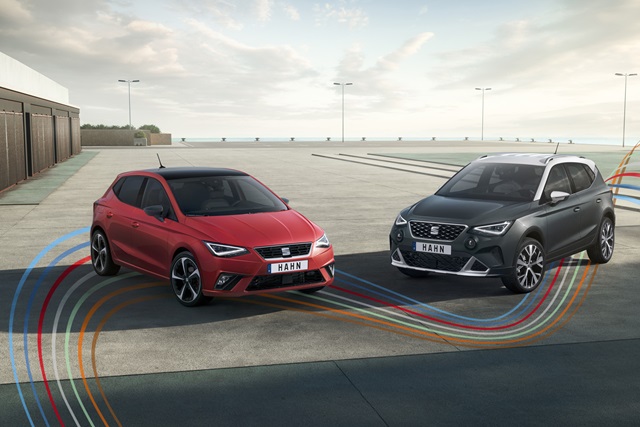 Ein roter SEAT Ibiza steht neben einem grauen SEAT Arona. Beide Fahrzeuge sind in Frontansicht auf einem Parkplatz zu sehen. 