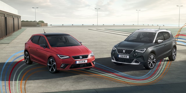 Ein roter SEAT Ibiza steht neben einem grauen SEAT Arona. Beide Fahrzeuge sind in Frontansicht auf einem Parkplatz zu sehen. 
