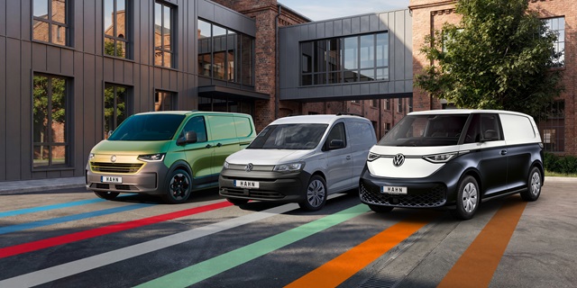 Drei nebeneinander geparkte Volkswagen Nutzfahrzeuge vor einem modernen Backsteingebäude von links nach rechts: ein Transporter, ein Caddy und ein ID. Buzz