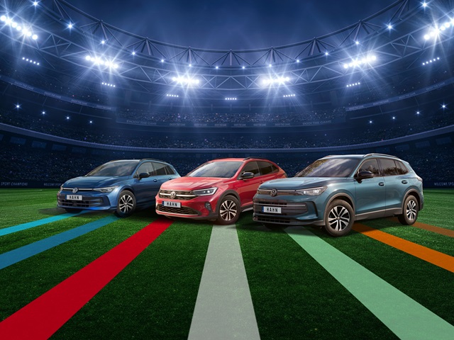 VW Golf Variant, Taigo und Tiguan in Blau, Rot und Grau stehen nebeneinander auf einem Fußballfeld unter Flutlicht in einem Stadion.