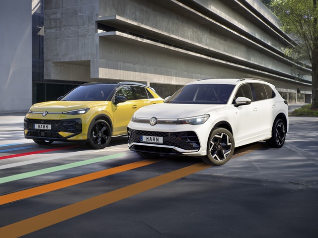 Gelber VW T-Roc R-Line und weißer VW Tiguan R-Line stehen nebeneinander vor einem Gebäude.