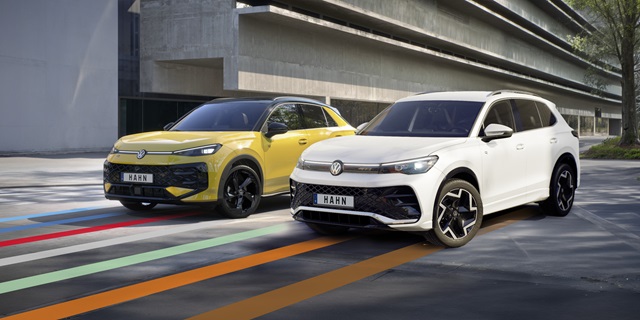 Gelber VW T-Roc R-Line und weißer VW Tiguan R-Line stehen nebeneinander vor einem Gebäude.