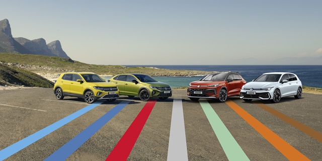 Vier verschiedene Volkswagen-Modelle nebeneinander auf einer Küstenstraße, im Hintergrund Meer und Berge.