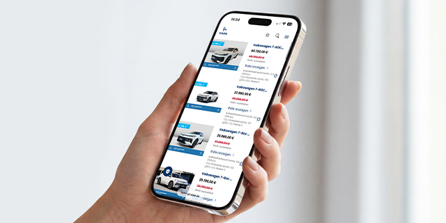 Hand hält Smartphone mit Fahrzeugbörse, die mehrere Fahrzeuge mit Bildern und Preisen zeigt.