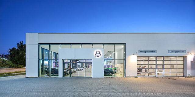 Fassade des modernen Volkswagen-Standorts in Kornwestheim mit beleuchtetem VW-Logo und zwei Bereichen mit der Aufschrift 'Dialogannahme'