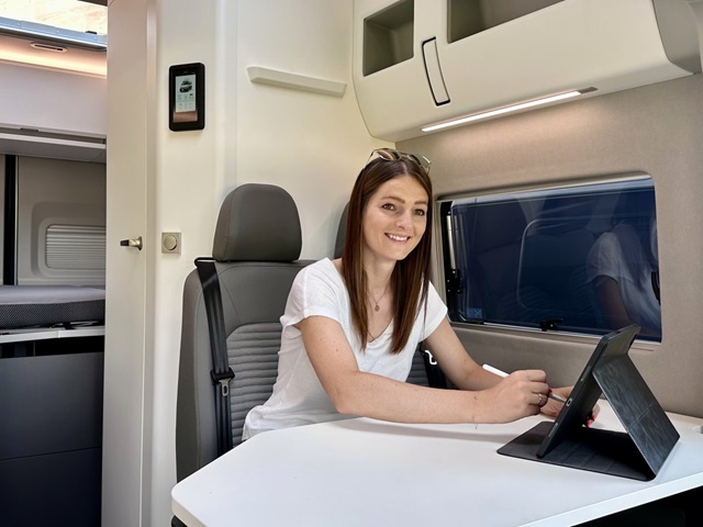 Eine Frau sitzt an einem Schreibtisch in einem VW Grand California und arbeitet konzentriert an ihrem Laptop.