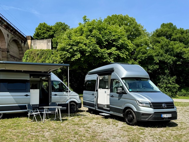 Der VW Grand California 600 und der VW Grand California 680 stehen vor Bäumen auf einer Wiese.