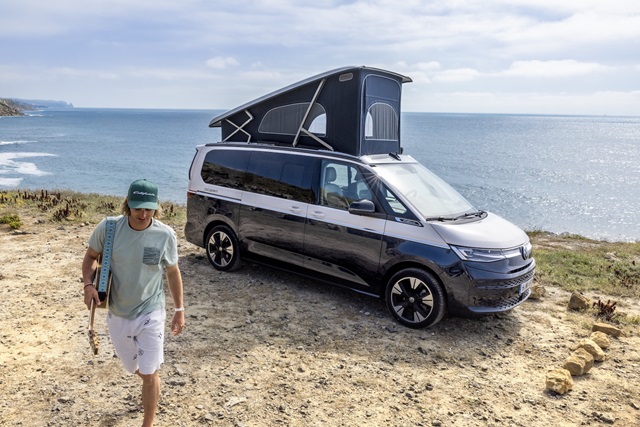 Der Volkswagen California Ocean an der Küste mit Aufstelldach. Davor ein Mann mit Gitarre.
