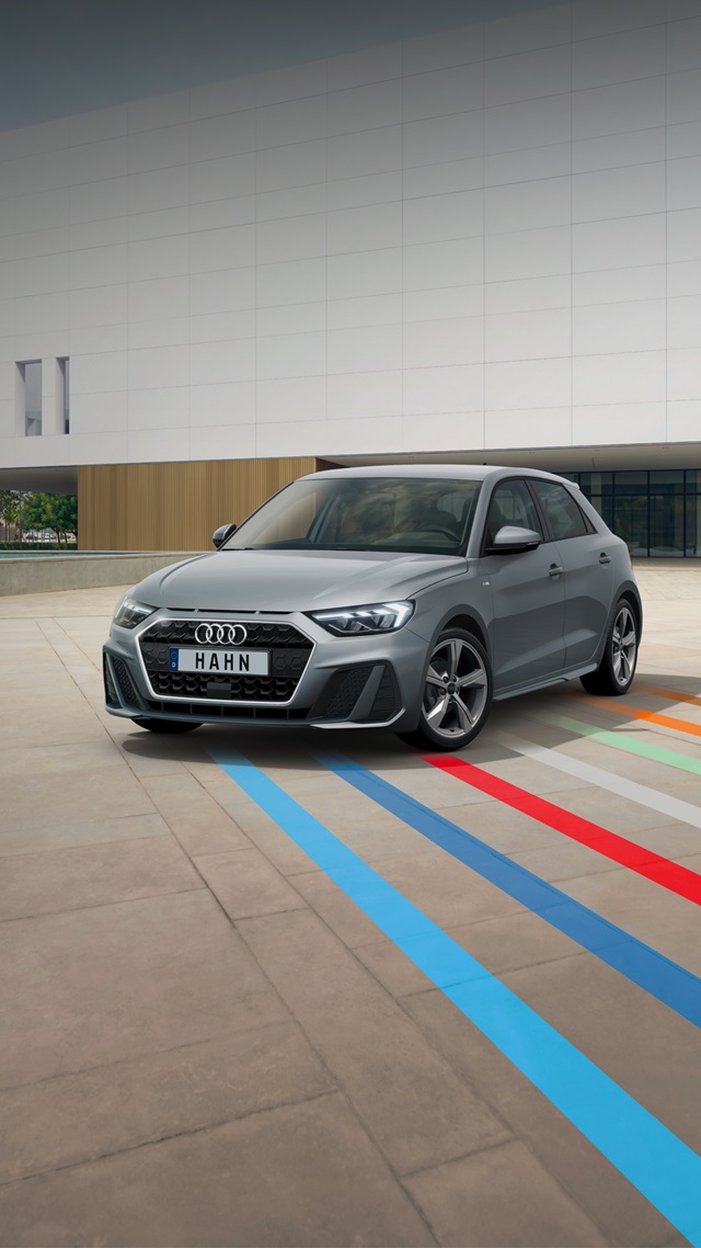 Grauer Audi A1 in Frontansicht auf gepflastertem Platz mit farbigen Linien vor modernem Gebäude