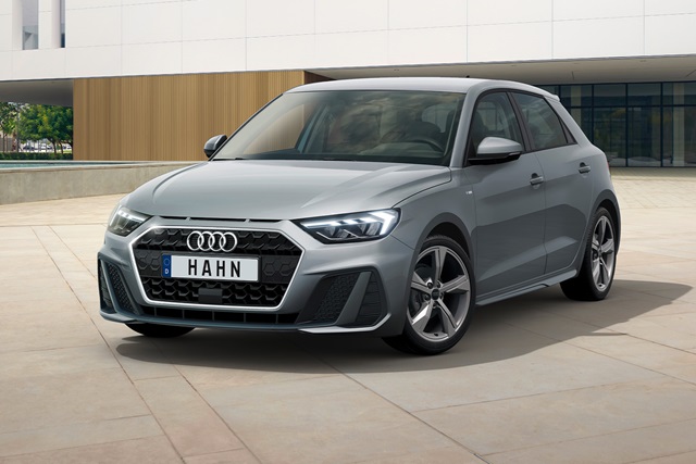 Grau lackierter Audi A1 in Frontansicht mit fünf Speichen Felgen und deutschem Kennzeichen 'HAHN' vor modernem Gebäude