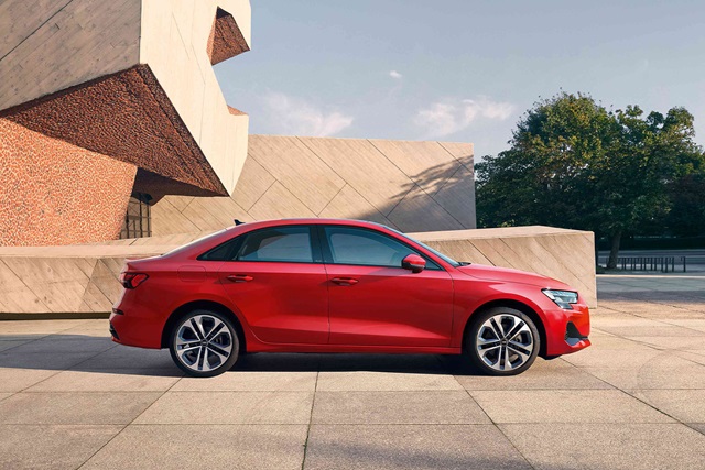 Rote Audi A3 Limousine in Seitenansicht vor modernem Gebäude und Bäumen
