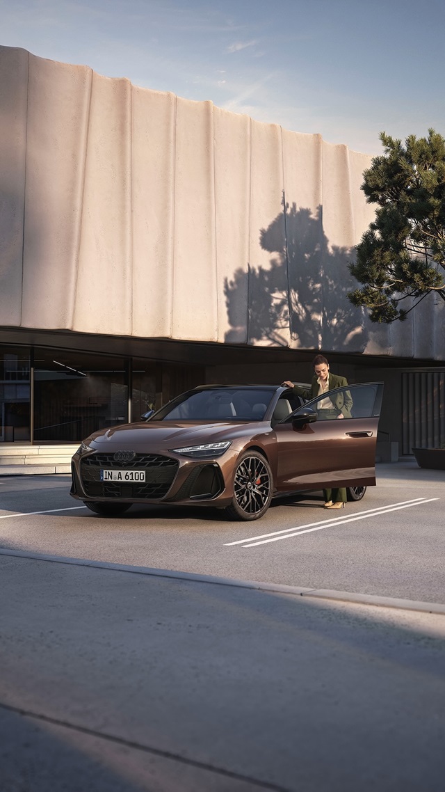 Der Audi A6 Avant parkend vor einem modernen Gebäude mit einer Person, die auf der Fahrerseite einsteigt. 