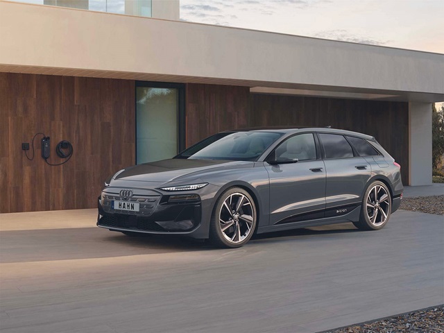 Seitenansicht eines grauen Audi A6 Avant E-Tron vor modernem Haus mit Ladestation an der Wand