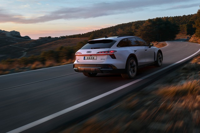 Weiße Audi A6 Allroad Hybrid-Heckansicht auf kurviger Landstraße bei Sonnenuntergang mit Wald im Hintergrund