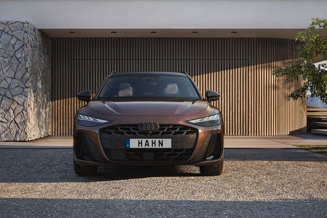 Brauner Audi A6 Avant von vorne mit schwarzem Kühlergrill und Nummernschild 'HAHN' vor moderner Fassade mit Holzlamellen und Steinwand