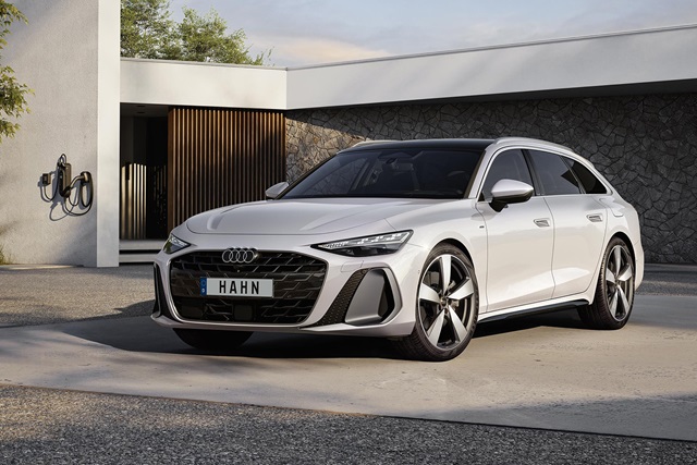 Weißer Audi A6 Avant Hybrid mit schwarzem Kühlergrill und großen Felgen vor modernem Haus mit Ladestation an der Wand