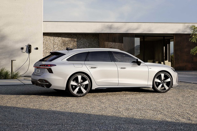 Weißer Audi A6 Avant Hybrid in Seitenansicht vor modernem Gebäude mit Ladestation an der Wand