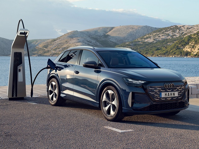 Blauer Audi Q4 e-tron SUV von vorne an Ladestation am Wasser mit Bergen im Hintergrund