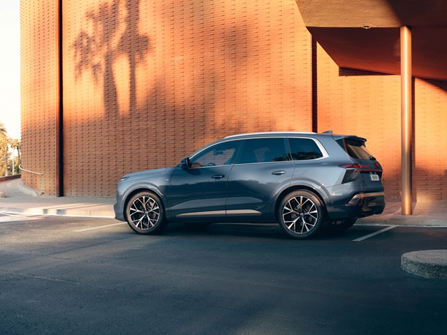 Seitenansicht eines blauen Audi Q7 vor einer orangefarbenen Wand mit Schatten von Bäumen