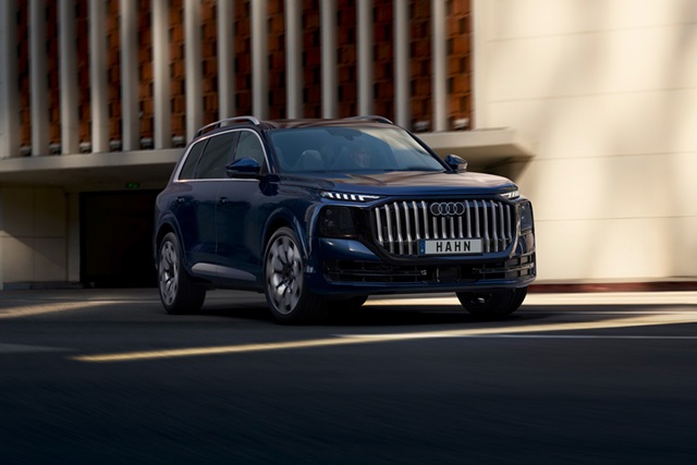 Blauer Audi Q9 SUV von vorne mit markantem Kühlergrill und dem Schriftzug 'HAHN' auf dem Nummernschild vor moderner Architektur