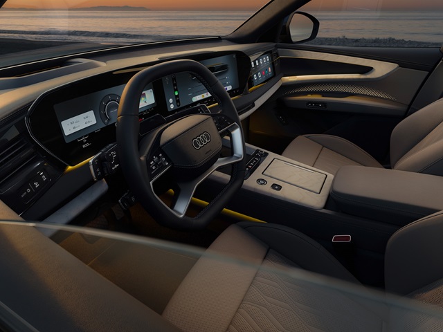 Innenraum des Audi Q9 mit digitalem Cockpit, großem Touchscreen, Lederlenkrad und beigen Ledersitzen bei Sonnenuntergang am Meer