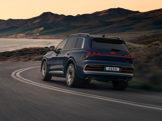 Heckansicht eines blauen Audi Q9 auf einer kurvigen Küstenstraße mit Berglandschaft im Hintergrund