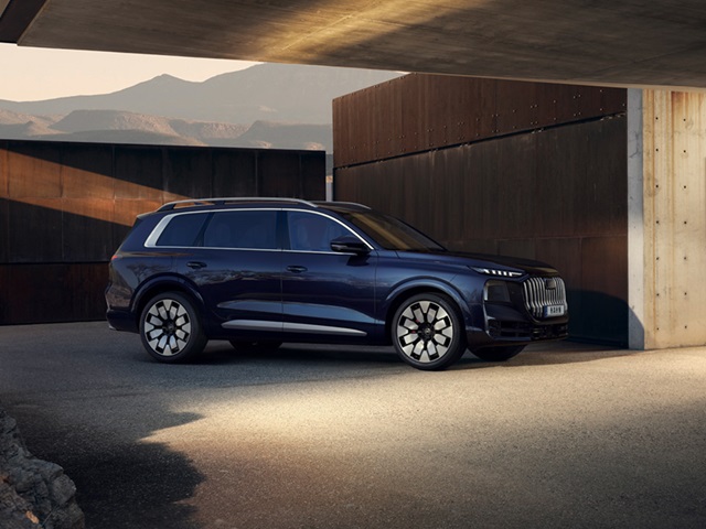 Blauer Audi Q9 SUV in Seitenansicht vor moderner Architektur mit klaren Linien und Bergkulisse im Hintergrund