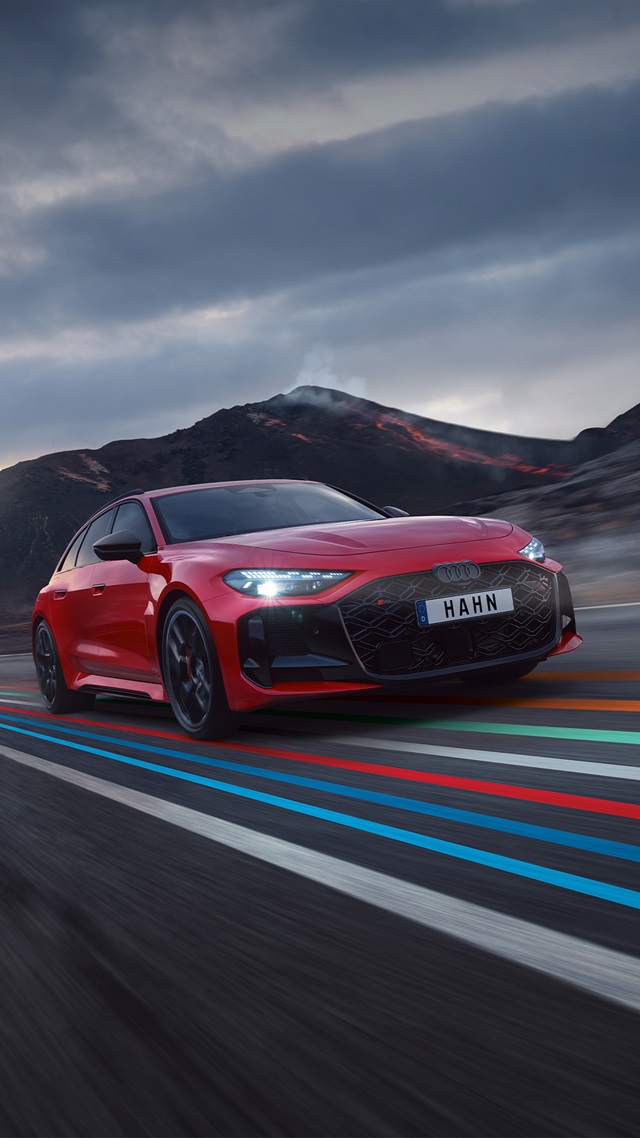 Roter Audi RS 5 Avant mit schwarzem Kühlergrill und HAHN-Kennzeichen fährt auf einer Straße vor bergiger Landschaft unter bewölktem Himmel