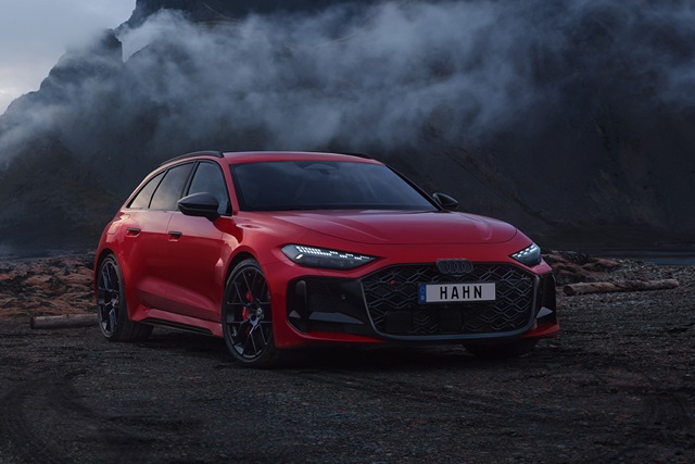 Roter Audi RS 5 Avant mit schwarzem Kühlergrill und schwarzem Dach in Frontansicht auf dunklem, felsigem Untergrund vor rauchigem, wolkigem Hintergrund