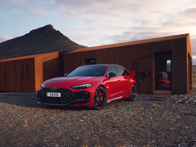 Roter Audi RS 5 Avant mit schwarzem Kühlergrill und schwarzen Felgen steht vor modernem, braunem Gebäude in bergiger Landschaft