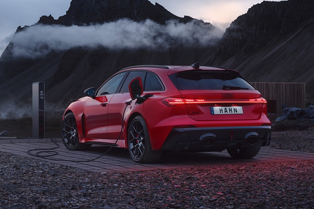 Roter Audi RS 5 Avant von hinten rechts an Ladestation in bergiger Landschaft bei Dämmerung