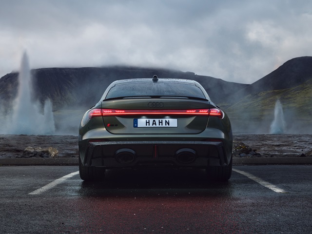 Heckansicht eines grünen Audi RS 5 Limousine mit Kennzeichen 'HAHN' vor einer Landschaft mit Wasserfontänen und bewölktem Himmel