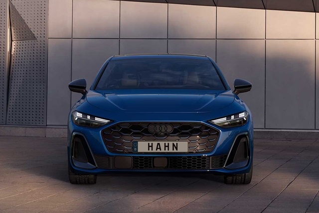 Blaue Audi S5 Limousine von vorne mit markantem Wabengrill und LED-Scheinwerfern vor einer modernen Wand
