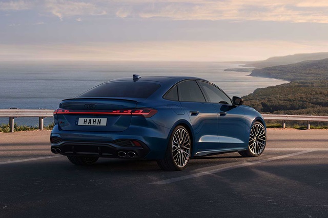 Blaue Audi S5 Limousine von hinten rechts auf einer Küstenstraße mit Meer und bewaldeten Hügeln im Hintergrund