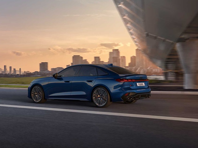 Blaue Audi S5 Limousine in Seitenansicht auf Straße mit moderner Stadt im Hintergrund und Brücke rechts