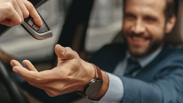 Mann übergibt Autoschlüssel an eine andere Person im Auto