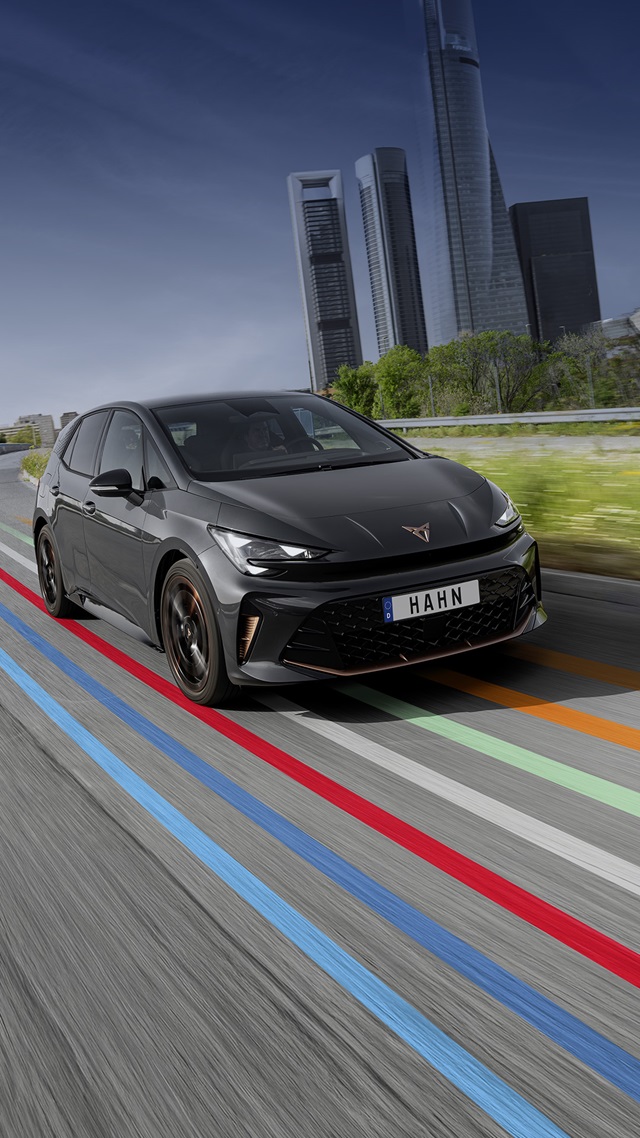 Dunkelgrauer CUPRA Born VZ fährt auf einer Straße mit farbigen Linien vor einer Skyline mit hohen Gebäuden