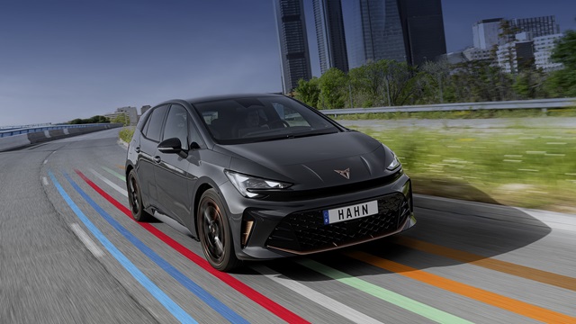 Dunkelgrauer CUPRA Born VZ fährt auf einer Straße mit farbigen Linien vor einer Skyline mit hohen Gebäuden