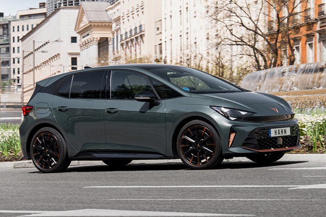 Seitenansicht eines CUPRA Born VZ mit sportlichen schwarzen Felgen und orangefarbenen Akzenten vor einem Springbrunnen in urbaner Umgebung