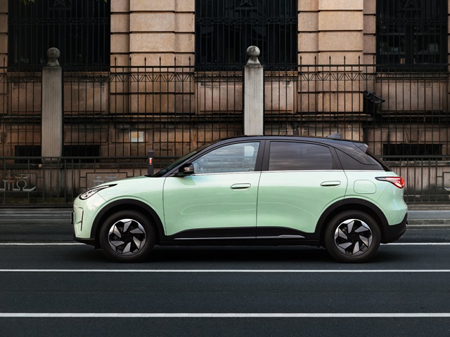 Geely E2 in minigrün in der Seitenansicht fährt auf einer Straße, im Hintergrund ein hellbraunes Gebäude