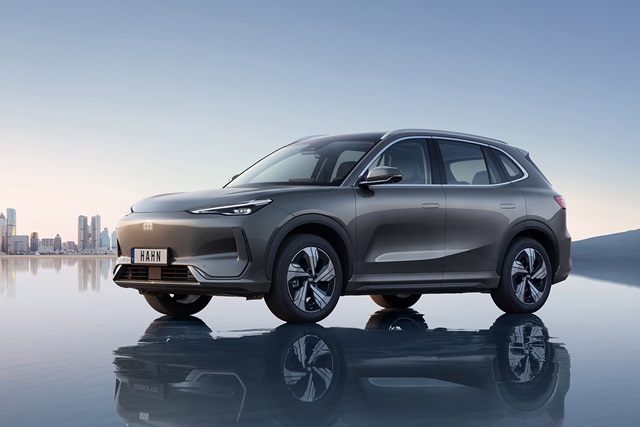 Seitenansicht eines dunkelgrauen Geely Starray EM-i SUV mit reflektierendem Boden und Stadtpanorama im Hintergrund