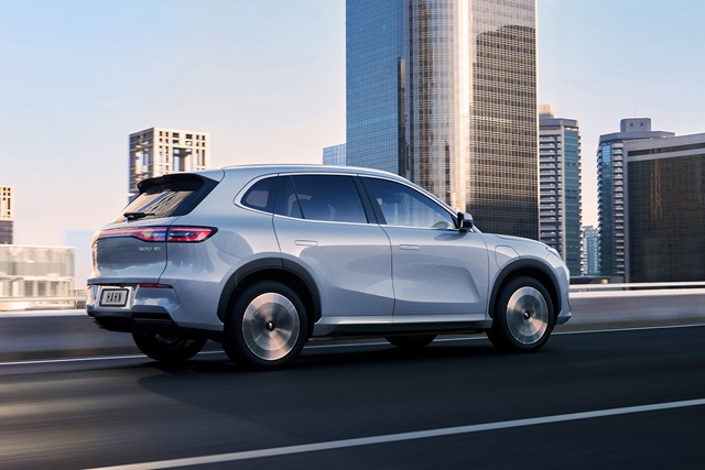 Silberfarbener Geely Starray EM-i SUV in Seitenansicht auf einer Straße vor Hochhäusern in der Stadt