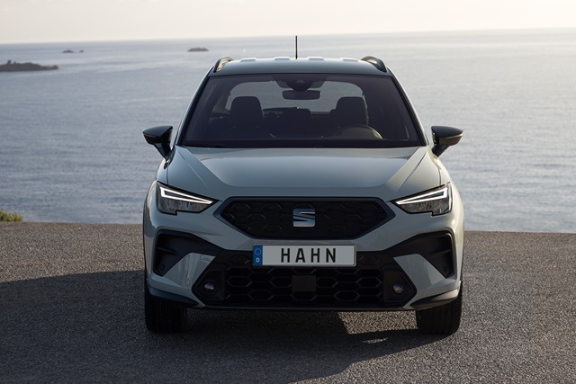 Frontansicht eines grauen SEAT Arona SUV mit schwarzem Kühlergrill und Kennzeichen 'HAHN' vor Meereshintergrund