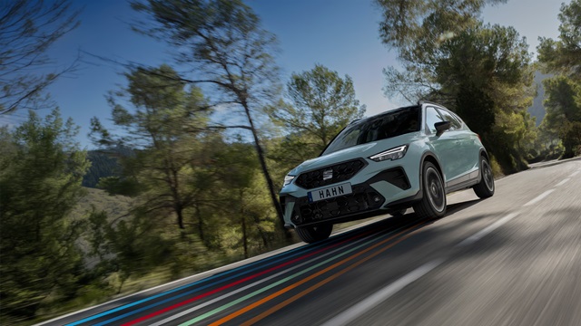 SEAT Arona SUV in Grau fährt auf einer Straße mit Bäumen im Hintergrund
