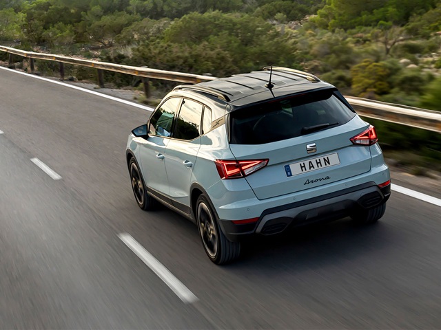 Heckansicht eines grauen SEAT Arona SUV mit geöffnetem Schiebedach auf einer Landstraße