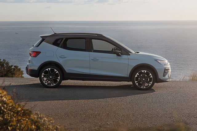 Seitliche Ansicht eines grauen SEAT Arona SUV auf einer Küstenstraße mit Meer im Hintergrund