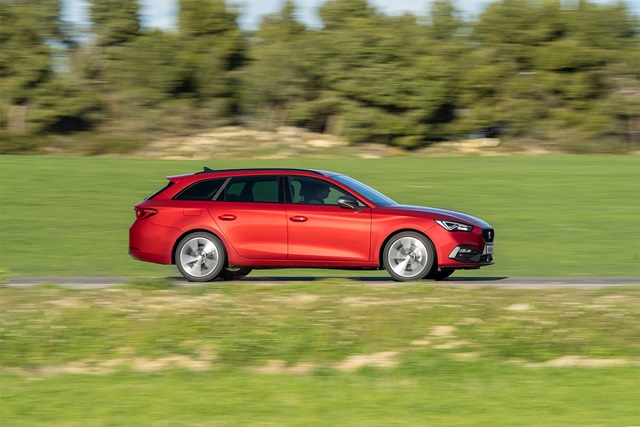 Roter SEAT Leon Sportstourer in Seitenansicht auf einer Straße mit grüner Wiese und Bäumen im Hintergrund